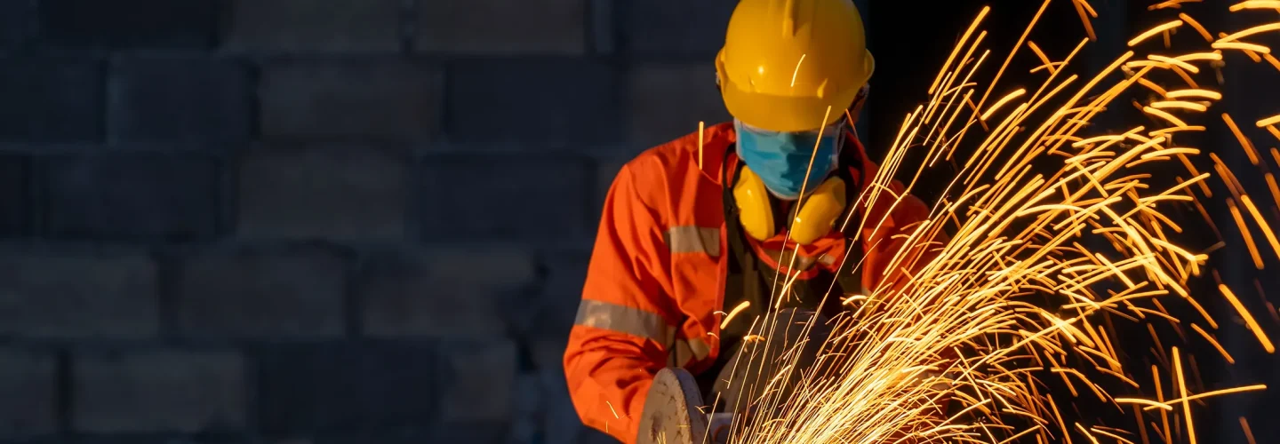 Industrial photo of man in orange coveralls grinding steel and sparks flying